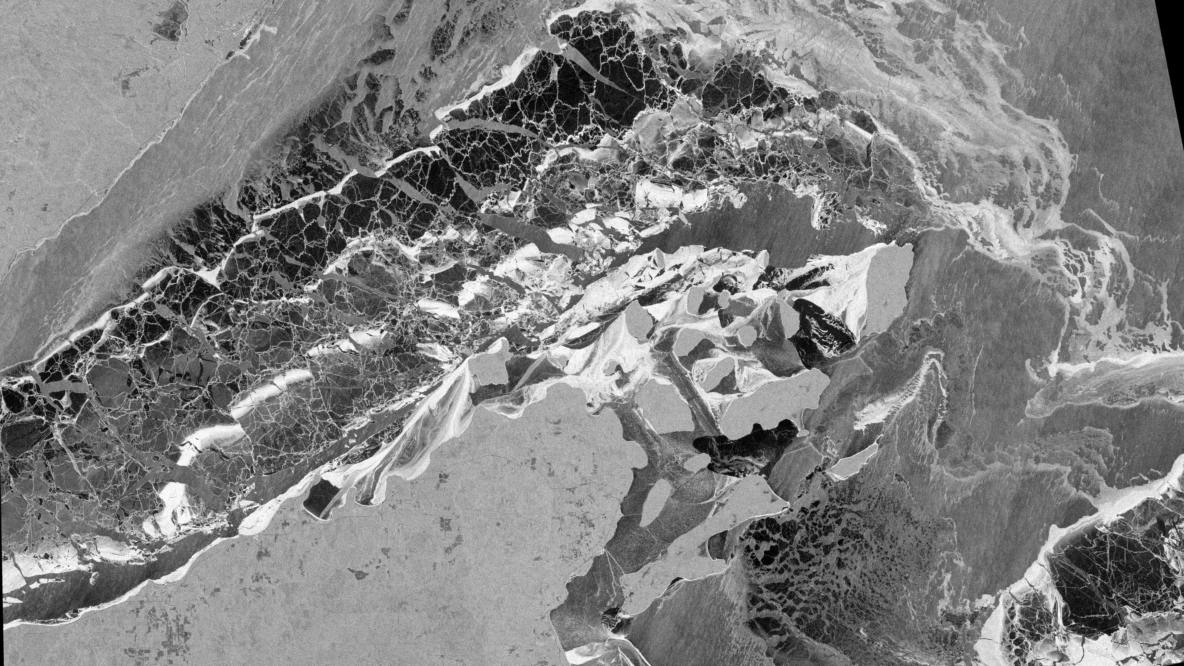Black and white radar satellite image of Lake Superior ice around the Apostle Islands, showing textured ice fields and dark water.