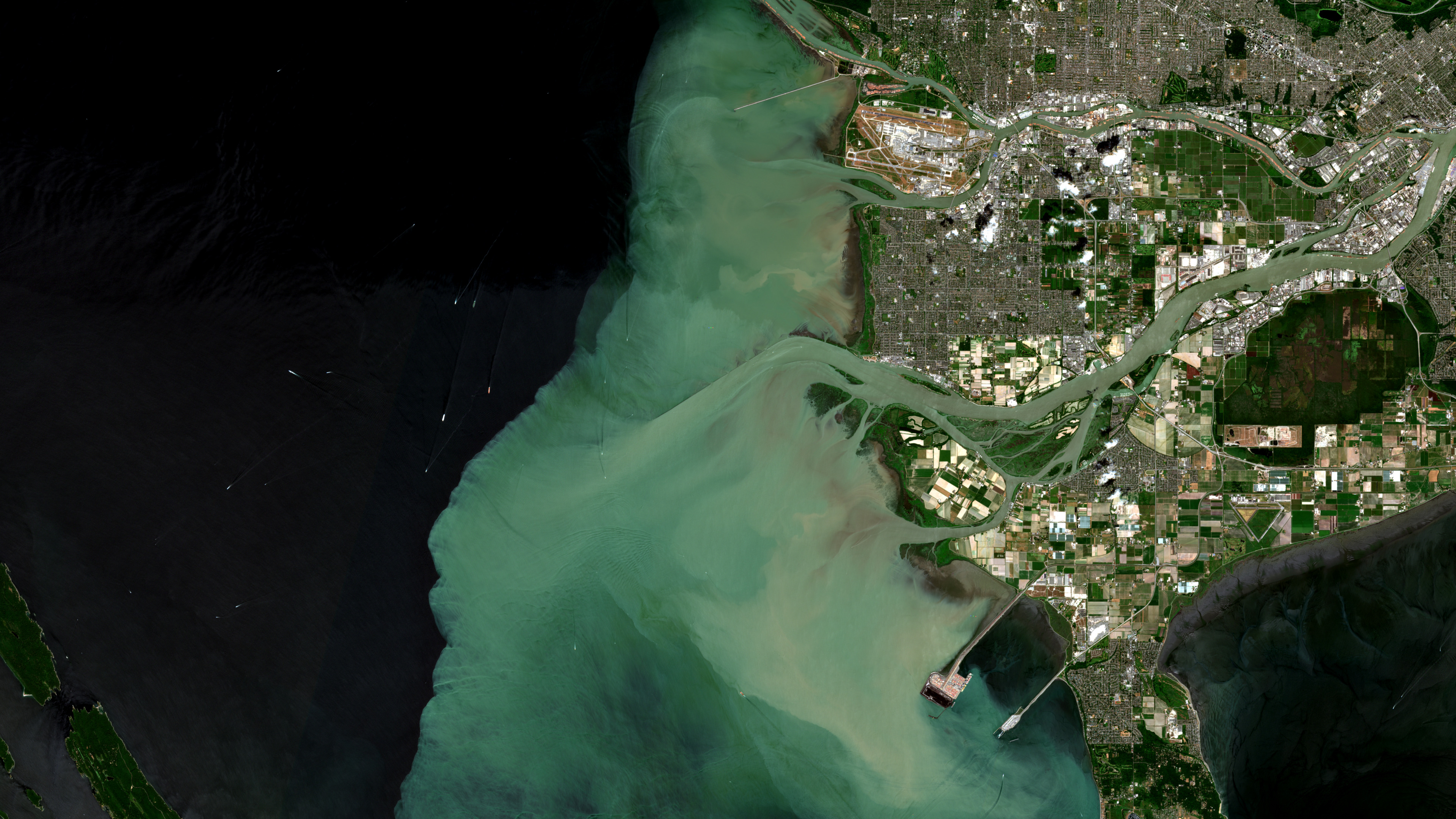 Satellite image of the Fraser River delta near Vancouver, with pale turquoise sediment-rich water spreading into dark coastal water beside islands, river channels, and urban shoreline.