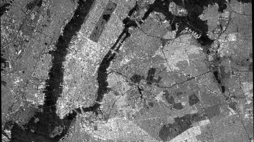 Black and white radar satellite image of Manhattan, New York, with the island glowing bright between dark surrounding rivers.