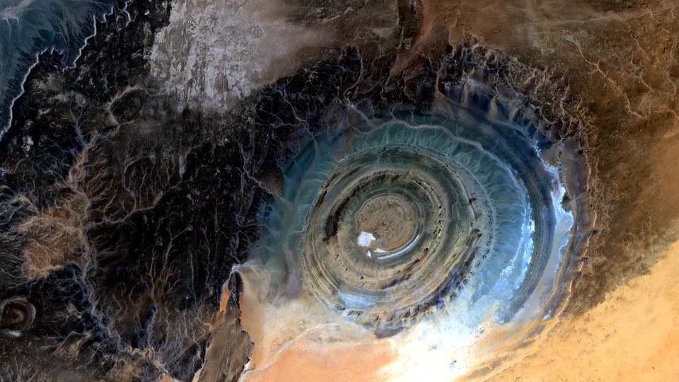 A natural-color Sentinel-2 satellite view of a large circular geologic structure in the Sahara, with blue-gray concentric rings surrounded by tan and gold desert.